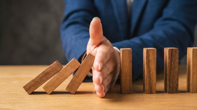 Businessman stopping falling dominoes to prevent crisis.