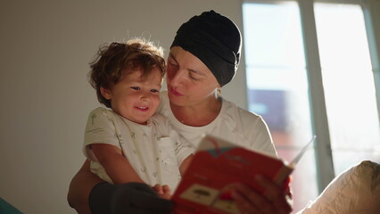 Excited toddler reacts joyfully as his mother reads a picture book and kisses him on the sofa at...