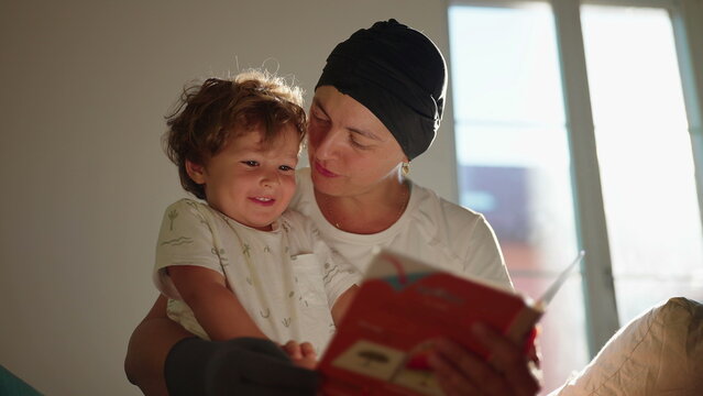 Excited toddler reacts joyfully as his mother reads a picture book and kisses him on the sofa at home, inspiring literacy, wonder, affection and family connection