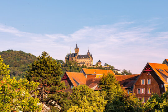 Scenic view of historic Wernigerode Castle on mountain above red tiled roofs of old town surrounded by green trees under blue sky, Germany travel concept