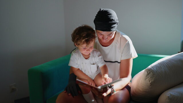 Mother reads an illustrated book with her toddler son seated on her lap on the sofa at home, promoting early literacy, focused education and close family connection