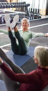 Vertical video: Female partners holding V-sit, senior lifting legs to start on mat in gym for core