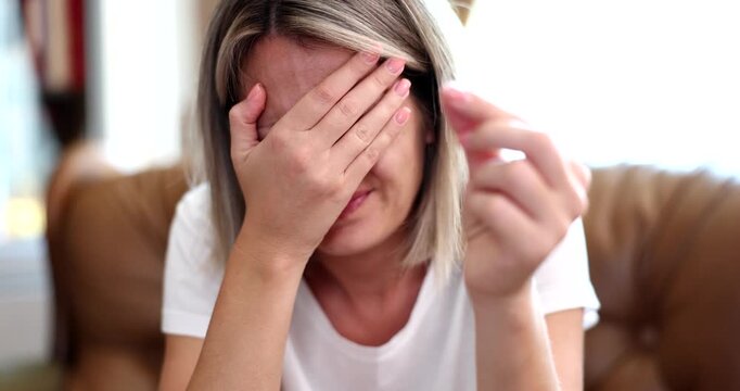 A woman sits thoughtfully in her cozy living room, experiencing a wave of emotions. She hides her face with her hands, deeply reflecting on her thoughts in the serene afternoon light.