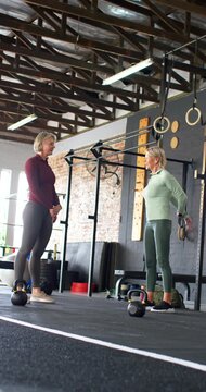 Vertical video: Women in gym chatting stretching placing hands on hips by kettlebells preparing