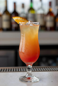 Refreshing tequila sunrise cocktail with an orange slice garnish and ice cubes on a bar counter, a vibrant tequila sunrise cocktail with a red and orange gradient is served in a hurricane glass
