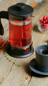 Close up view of a glass beverage dispenser filled with deep red liquid, resting on rustic weathered wooden planks for a warm aesthetic feel, perfect for summer refreshment shots