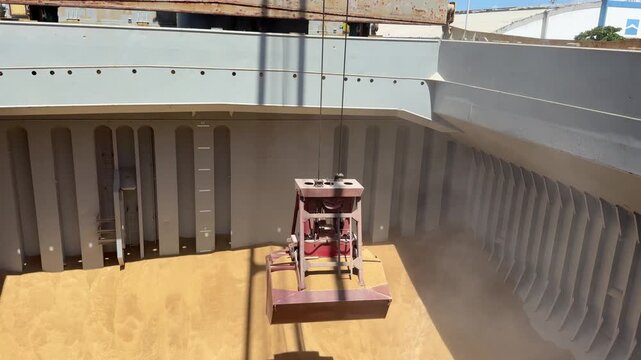 crane grab lifting cargo of malt in bulk from ship cargo hold.