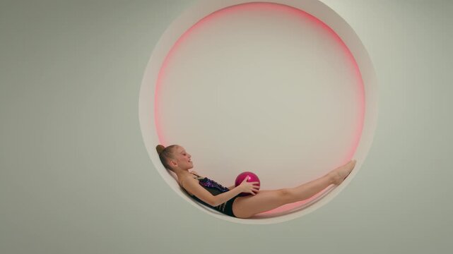 Little girl gymnast acrobat dancer child throwing gymnastic ball in white studio happy Caucasian female schoolgirl kid athlete relaxing sport ballet artistic gymnastics exercise having fun training