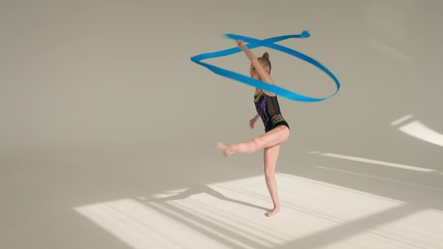 Sportive young little girl ballerina gymnast dancer swirling spinning with gymnastic ribbon in dance school Caucasian female child schoolgirl kid acrobat exercising dancing sport ballet indoor studio