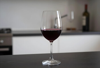 Fototapeta premium Glass of red wine on a dark kitchen counter with a blurred background, elegant beverage for celebration and relaxation