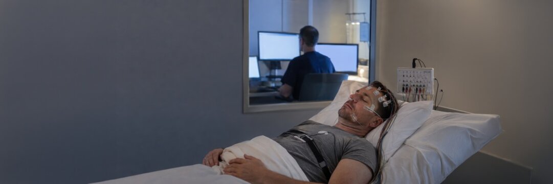 Man undergoes monitored sleep study with EEG electrodes in clinic, polysomnography and sleep disorder diagnostics