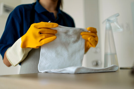 Professional Asian Female Cleaner Wearing Yellow Protective Gloves and Holding a Microfiber Cloth and Spray Bottle for Household Surface Cleaning and Hygiene Maintenance