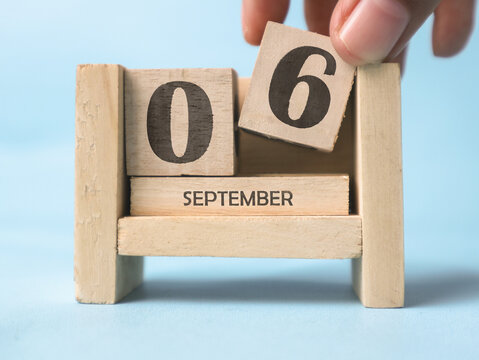 A woman's hand is holding a wooden block with the number 6 written on it on a wooden block calendar for September 6th on a light blue background.