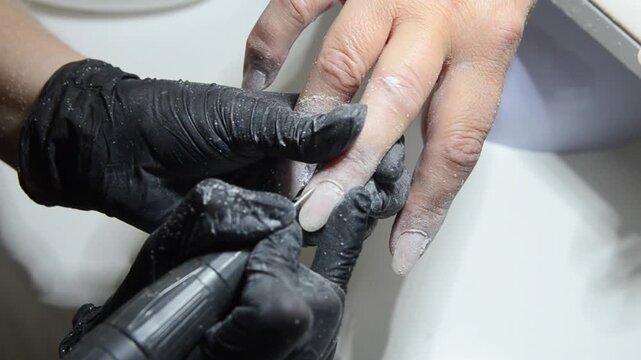 Professional manicurist removing cuticle with an electric nail drill during a hardware manicure. Close-up of nail preparation and cuticle care in a beauty salon.