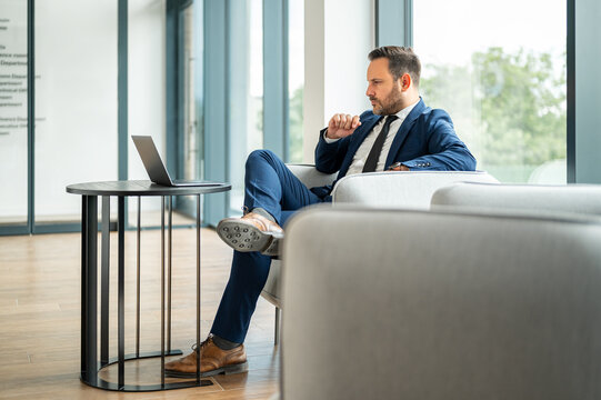 Business executive contemplating strategy while working remotely on a laptop, analyzing financial data and legal documents in a contemporary office lounge