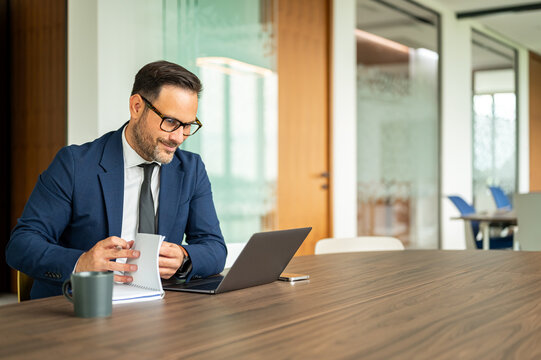 Business professional is reviewing documents and working on a laptop at a conference table, engaging in corporate operations, legal services, and financial management