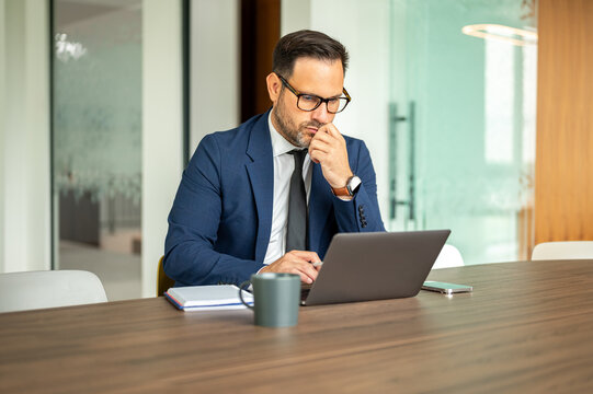 Professional businessman in blue business attire working on laptop in a contemporary office environment. Analyzing financial data and legal documents