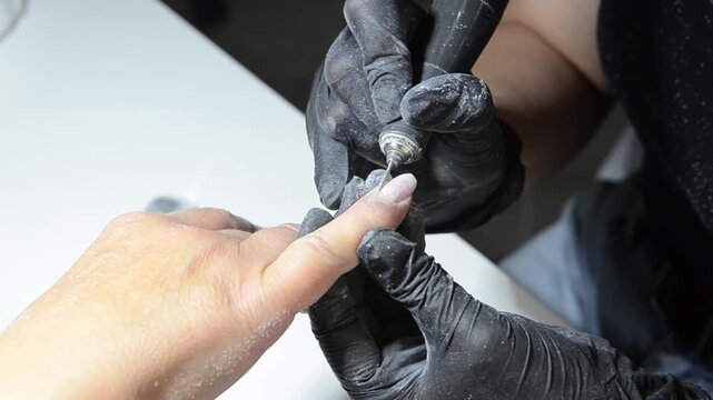 Professional manicurist removing cuticle with an electric nail drill during a hardware manicure. Close-up of nail preparation and cuticle care in a beauty salon.