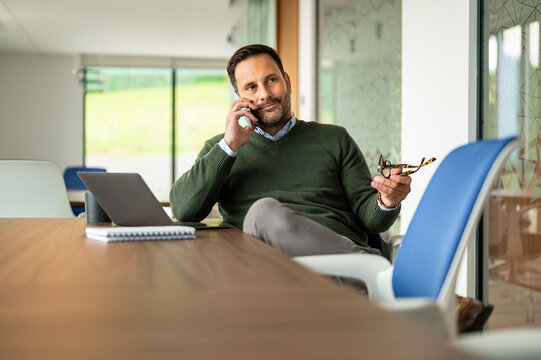Mature businessman communicating on phone in a modern office, planning strategies for corporate growth and leadership advancement while engaging in a confident conversation