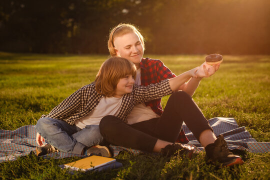 older brother teasing and treating little brother with delicious donut during picnic outdoors