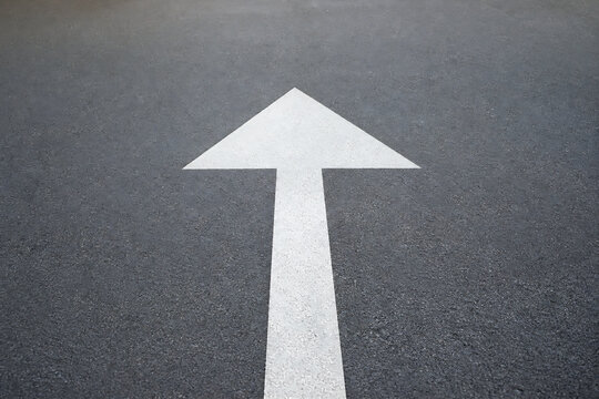 A white upward arrow painted on a dark asphalt road surface.