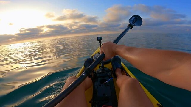 POV of man paddling a fishing kayak at sea during sunset