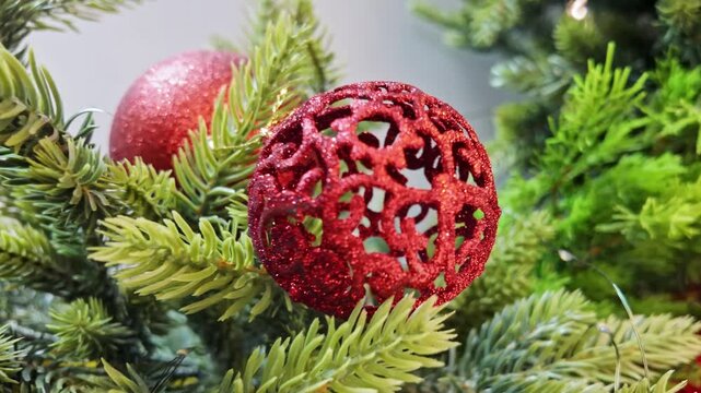 Macro shot of a red glittery lace christmas ball ornament hanging on fresh green pine tree.