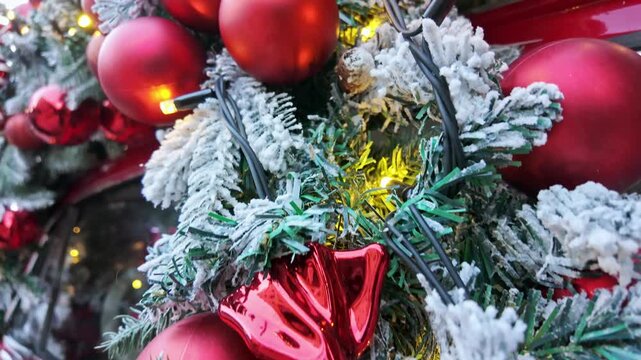 Closeup of glossy red christmas baubles and ornaments nestled on snow covered pine branches with lights.