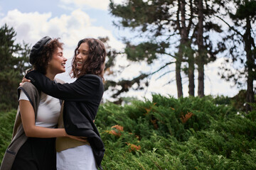 Fototapeta premium Young women embrace in vibrant green park on sunny day