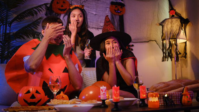 Young Asian friends reacting with surprise during a spooky Halloween party at home.