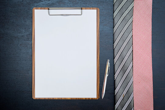 Blank report paper on wooden clipboard with pen and necktie on black background, business concept background