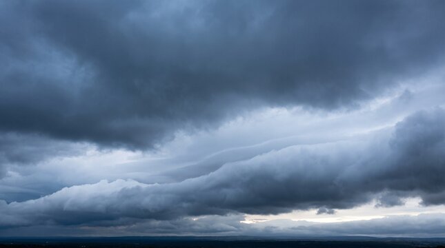 Dramatic storm clouds with horizon light breaking through heavy gray sky creating stark contrast over flat dark landscape