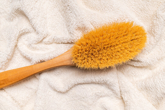 Massage brush with natural bristles on white cotton terry towel creates clean spa imagery for body care, wellness branding, home routines, personal grooming, and beauty product marketing.