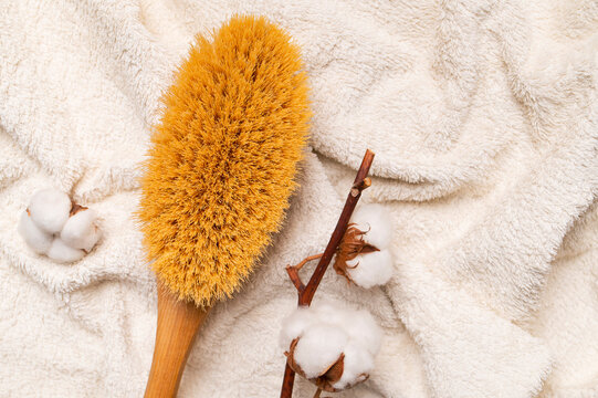 Massage brush with natural bristles, wooden handle and cotton twig on light terry towel top view. Concept: body care, spa treatments, brush for at-home dry massage against cellulite.
