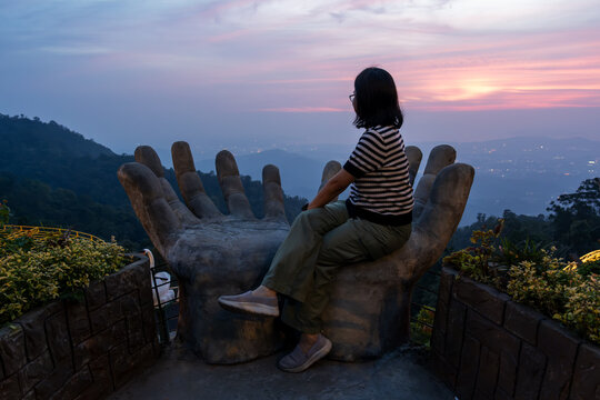 Woman sitting on a Buddha hand looking over sunset in Bukit Kokol Kota Kinabalu Sabah