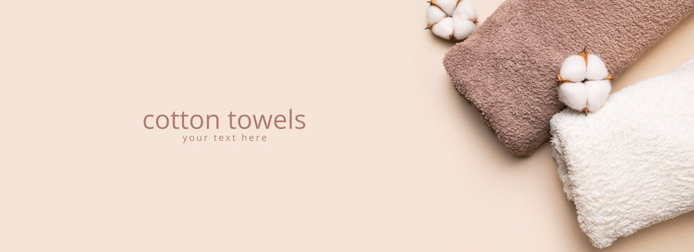 Folded cotton towels and white cotton flowers on beige background create calm spa styling. Soft textile, natural fibers and clean bath accessories support wellness, hotel and home care marketing.