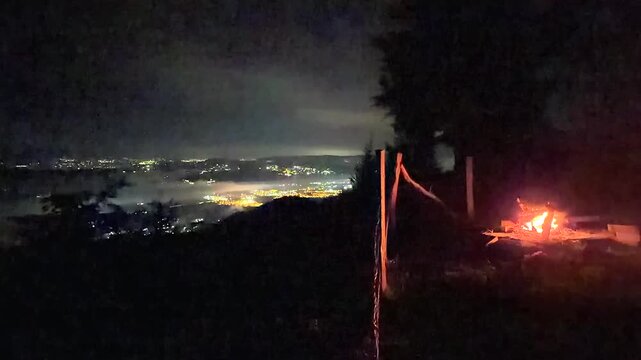 night view of campfire and illuminated city under fog and clouds