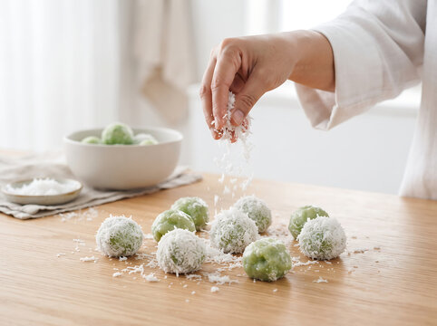 Hand sprinkling grated coconut on Indonesian klepon cake on a wooden table, traditional Asian sweet dessert rice balls, food photography