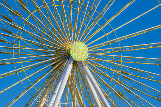 Close up of the Spokes of a Bright Yellow Ferris Wheel with a Blue Sky