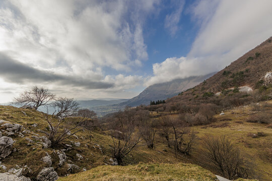 ampia vista panoramica su di un ambiente naturale tra le colline e le montagne della Slovenia centro-occidentale, di giorno, con cielo parzialmente nuvoloso, in primavera