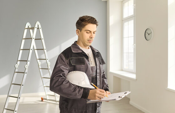 Contractor builder worker completing repair checklist on clipboard. Inspector in uniform holds helmet and writes renovation notes in room with ladder. Clear concept of renovation planning.