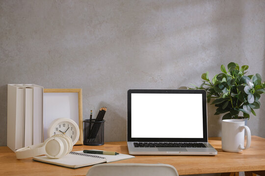 Modern home office workspace with laptop mockup screen, calculator, notebook, headphones, coffee cup and stationery on wooden desk.