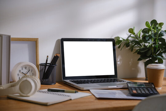 Modern home office workspace with laptop mockup screen, calculator, notebook, headphones, coffee cup and stationery on wooden desk.