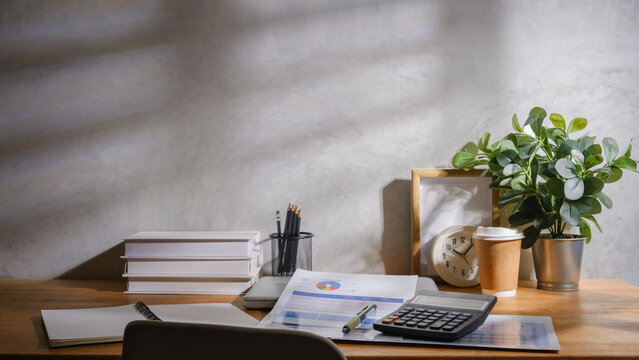 Financial workspace with calculator, budget report, pen, notebook, and laptop on a wooden desk in natural light.