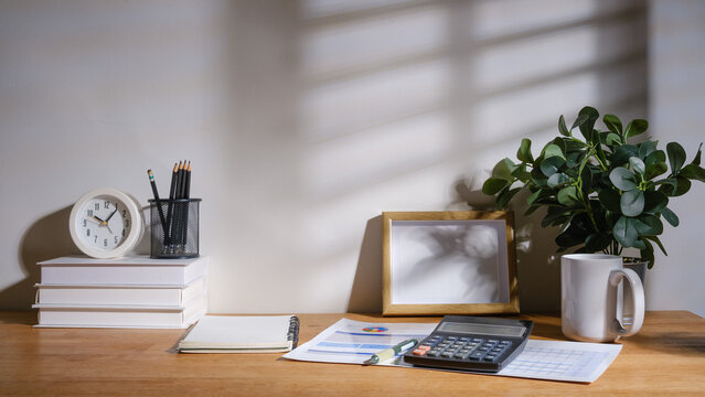 Financial workspace with calculator, budget report, pen, notebook, and laptop on a wooden desk in natural light.