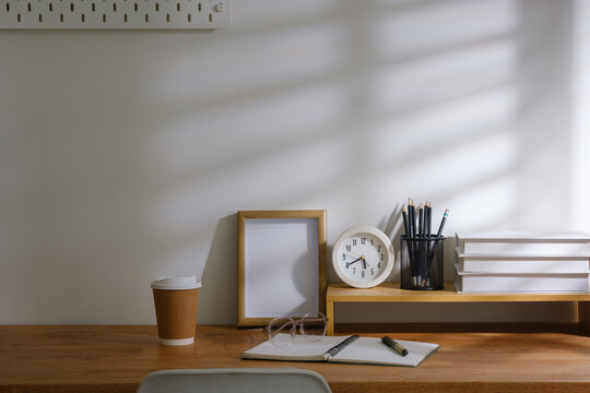 Cozy workspace scene featuring stationery, takeaway coffee, books and clock on a wooden desk, ideal for study, planning and productivity concepts.