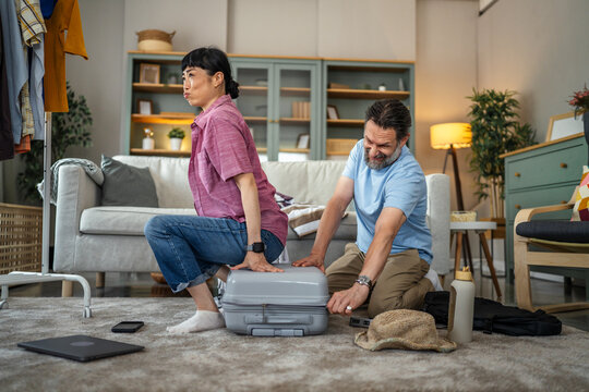 Couple struggling to close an overpacked suitcase for vacation