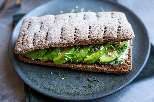 Close-up of crunchy rye flatbread sandwich with avocado and sesame.