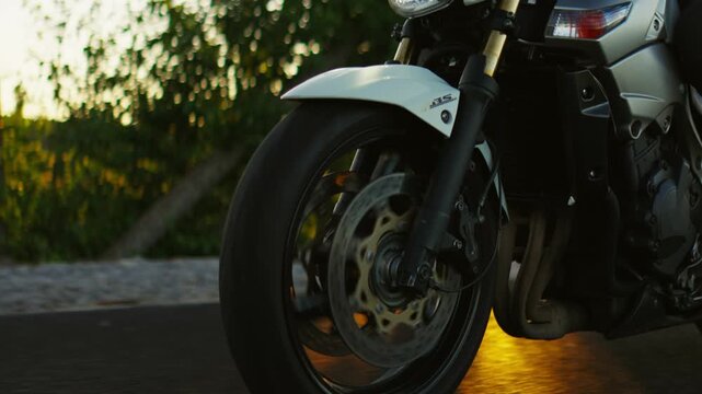 Sport motorcycle rider cruising along a forest road at sunset, close up of front wheel, headlight and protective gear capturing motion and evening atmosphere