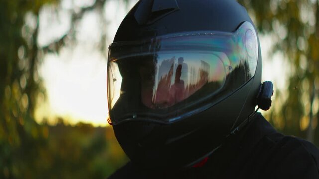 Motorcyclist wearing sleek black full-face helmet with reflective visor riding outdoors at sunset, capturing dramatic light, safety gear, and focused adventure mood